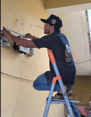 Workers lifting a solar panel onto a mounting structure beside a house